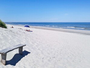 A sandy beach with a wooden bench and a blue umbrella.