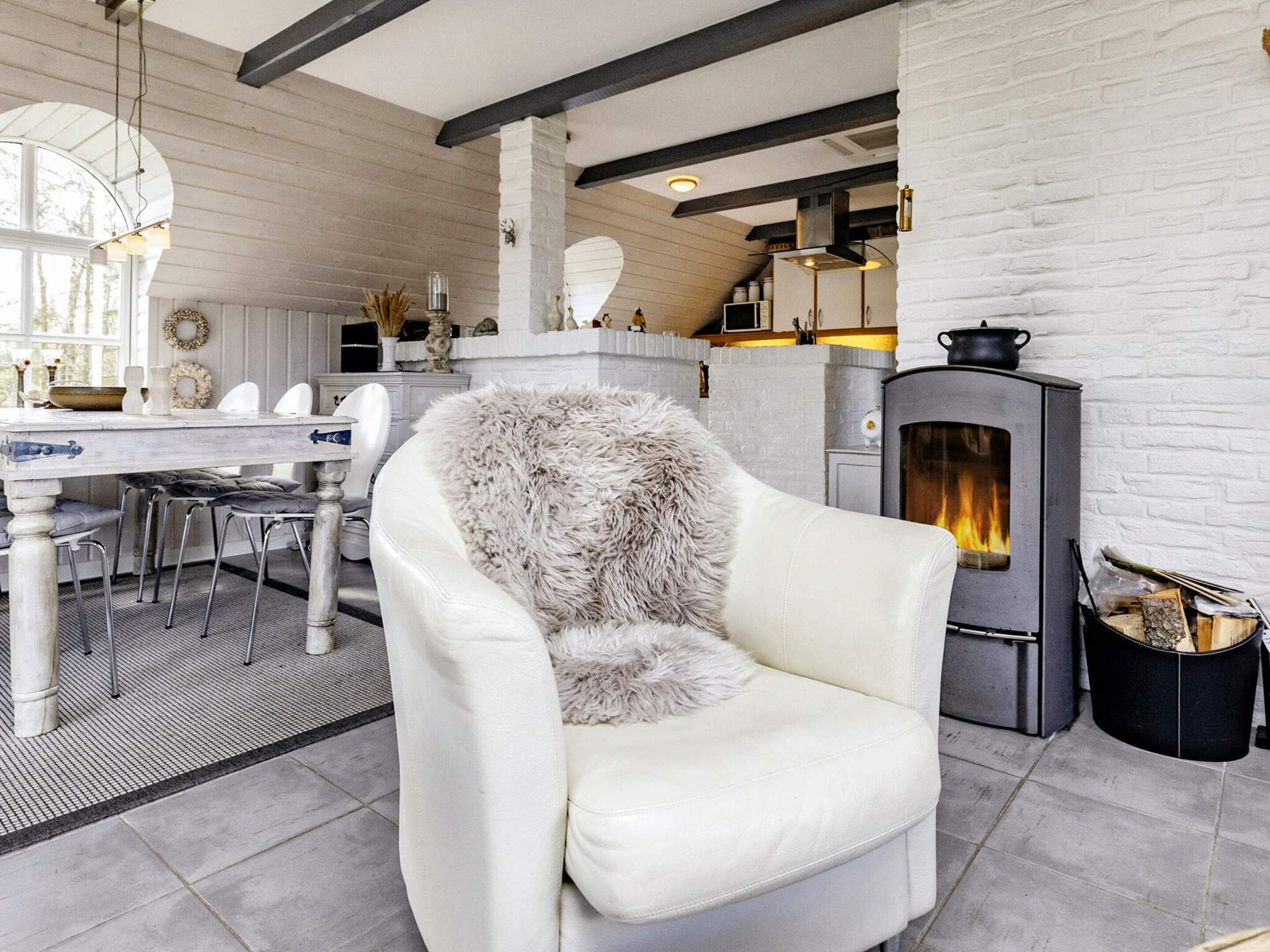 A cozy living room with a white leather armchair, a fireplace, and a dining area with a white table and chairs.