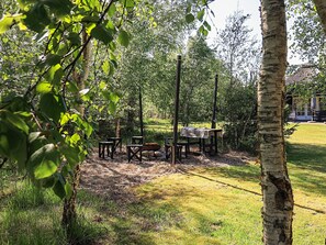 An outdoor seating area with tables and chairs, surrounded by trees and a grassy lawn. - Unique Pet Friendly Holiday Home in Jerup near Sea (Jerup)