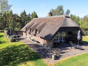 Un bâtiment à toit de chaume, avec une façade en briques, un espace extérieur aménagé pour s’asseoir et un jardin.