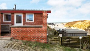 A small brick building with a red roof, a window, and a door. There is a wooden fence and a paved area in front. - Beachfront Bungalow Bliss - By Traum Ferienwohnungen (Henne)