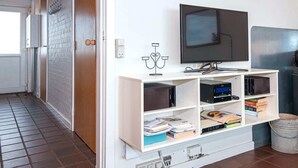 A modern living room with a flat-screen TV, built-in shelves with books and electronics, a fireplace, and a wooden door. - Beachfront Bungalow Bliss - By Traum Ferienwohnungen (Henne)