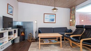 A cozy living room with a fireplace, sofa, and chairs, a TV, and a bookshelf. - Beachfront Bungalow Bliss - By Traum Ferienwohnungen (Henne)