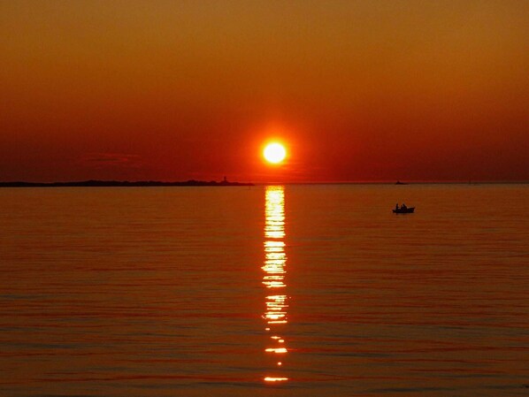 A sunset over a calm sea with a boat in the distance. - Holiday Home in Laukvik (Hadsel)