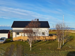 A house with a wooden deck, a flagpole, and a car parked in front.