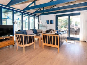 Un salón amplio con mobiliario de madera, televisor y ventanas grandes.