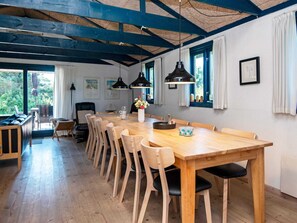 Un comedor con una larga mesa de madera, varias sillas, lámparas colgantes y vistas al exterior a través de amplios ventanales.