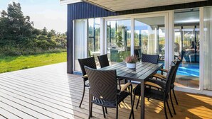 En udendørs terrasse med et bord og stole, store skydedøre og udsigt til en swimmingpool.