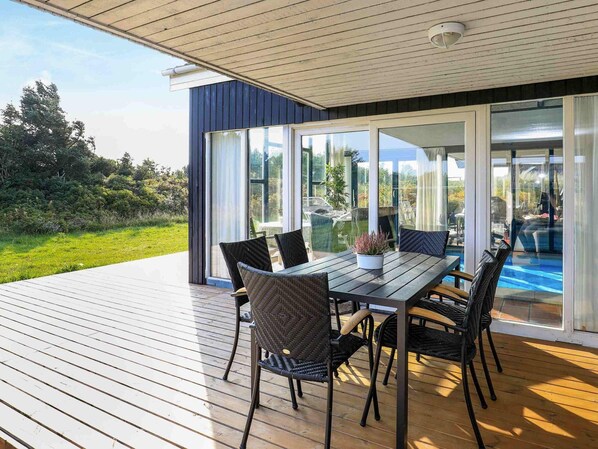 An outdoor deck with a table and chairs, large sliding glass doors, and a view of a swimming pool.