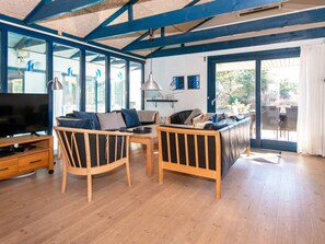 A modern living room with a TV, wooden furniture, and large windows. - 5 Star Holiday Home in Ringkobing (Ringkobing)