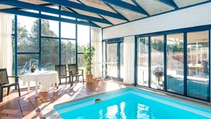 En swimmingpool med flisegulv og et overdækket område med stole og et bord.