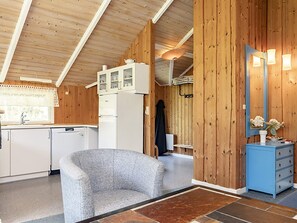 A compact kitchen with white appliances, a grey armchair, and a blue dresser.