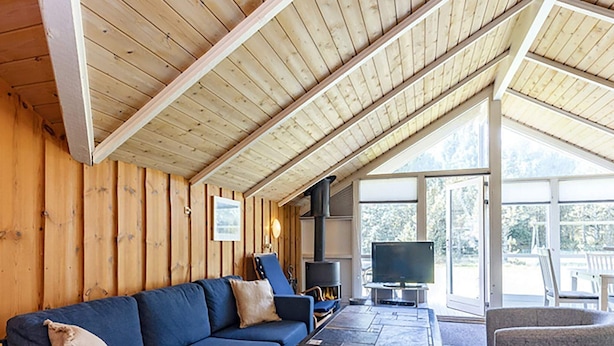 A cozy room with a wooden ceiling, a blue sofa, a table, and a TV. - 7 Person Holiday Home in Blavand (Blavand)