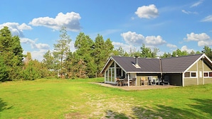 A single-story house with a large deck, surrounded by a grassy yard and trees. - 7 Person Holiday Home in Blavand (Blavand)
