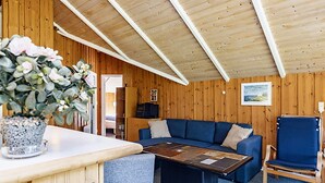 A cozy cabin interior with a wooden ceiling, a blue sofa, a small table, and a potted plant. - 7 Person Holiday Home in Blavand (Blavand)