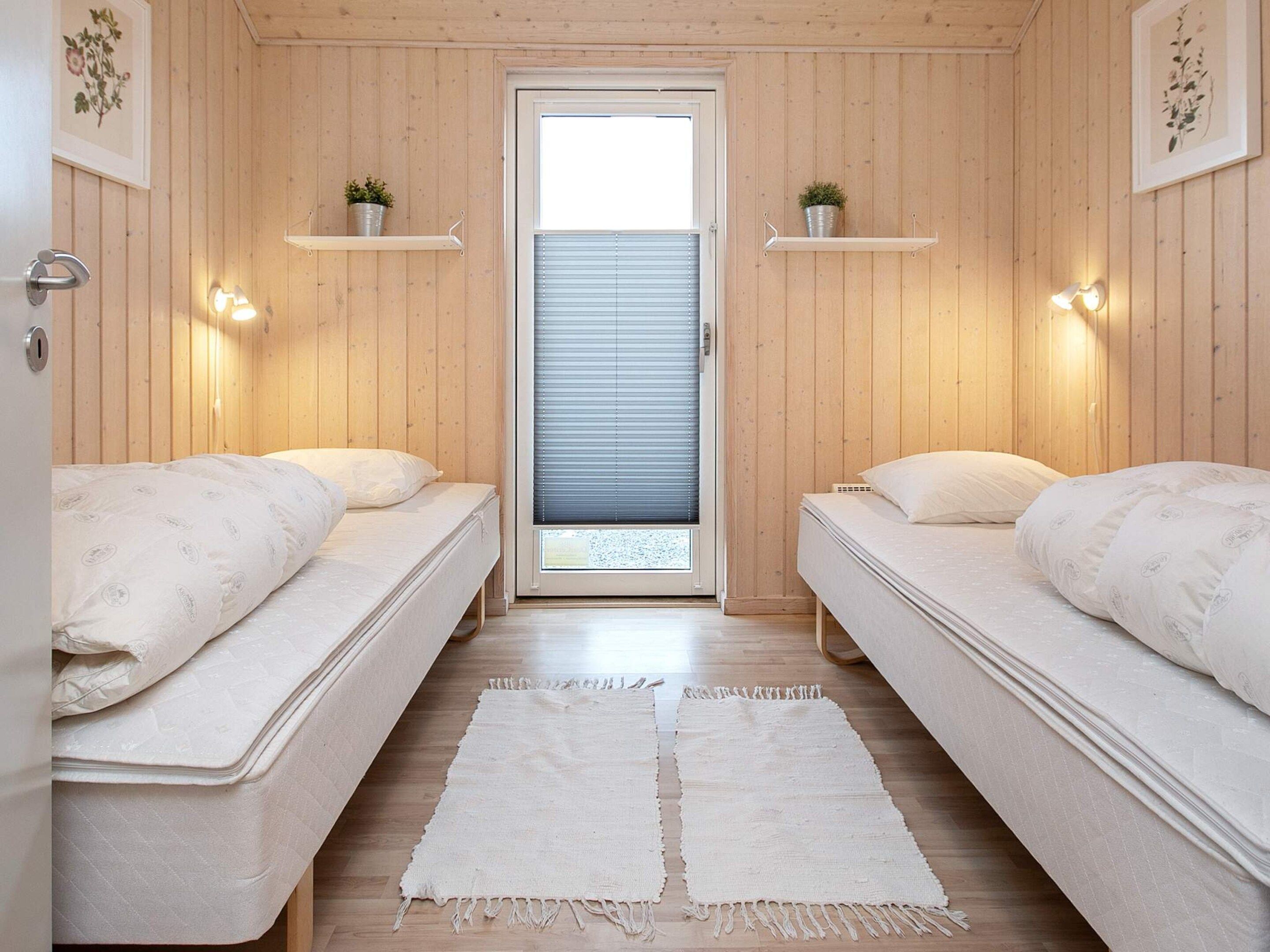 A room with two beds, a door with blinds, and wall-mounted shelves with plants.