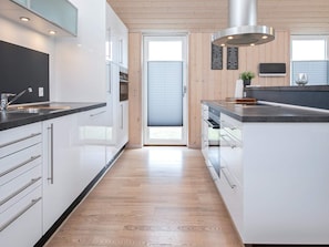 A modern kitchen with white cabinetry, a stainless steel sink, and a wooden floor. - 4 Star Holiday Home in Vaeggerlose (Vaeggerlose)