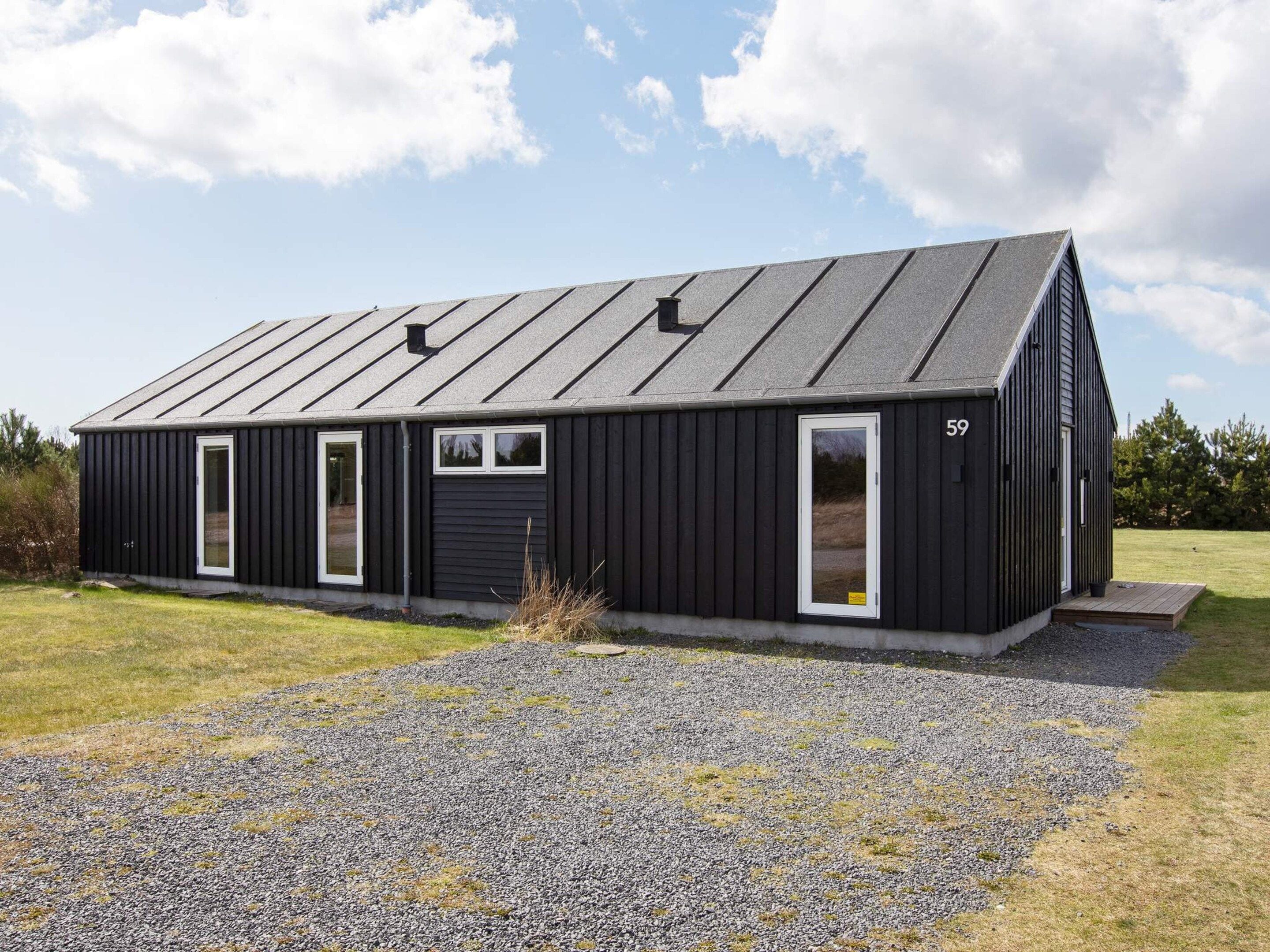 A black metal building with a sloped roof, numbered 59, and a gravel driveway.