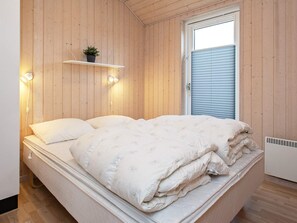 A bedroom with a bed, a shelf with a plant, and a window with blinds.