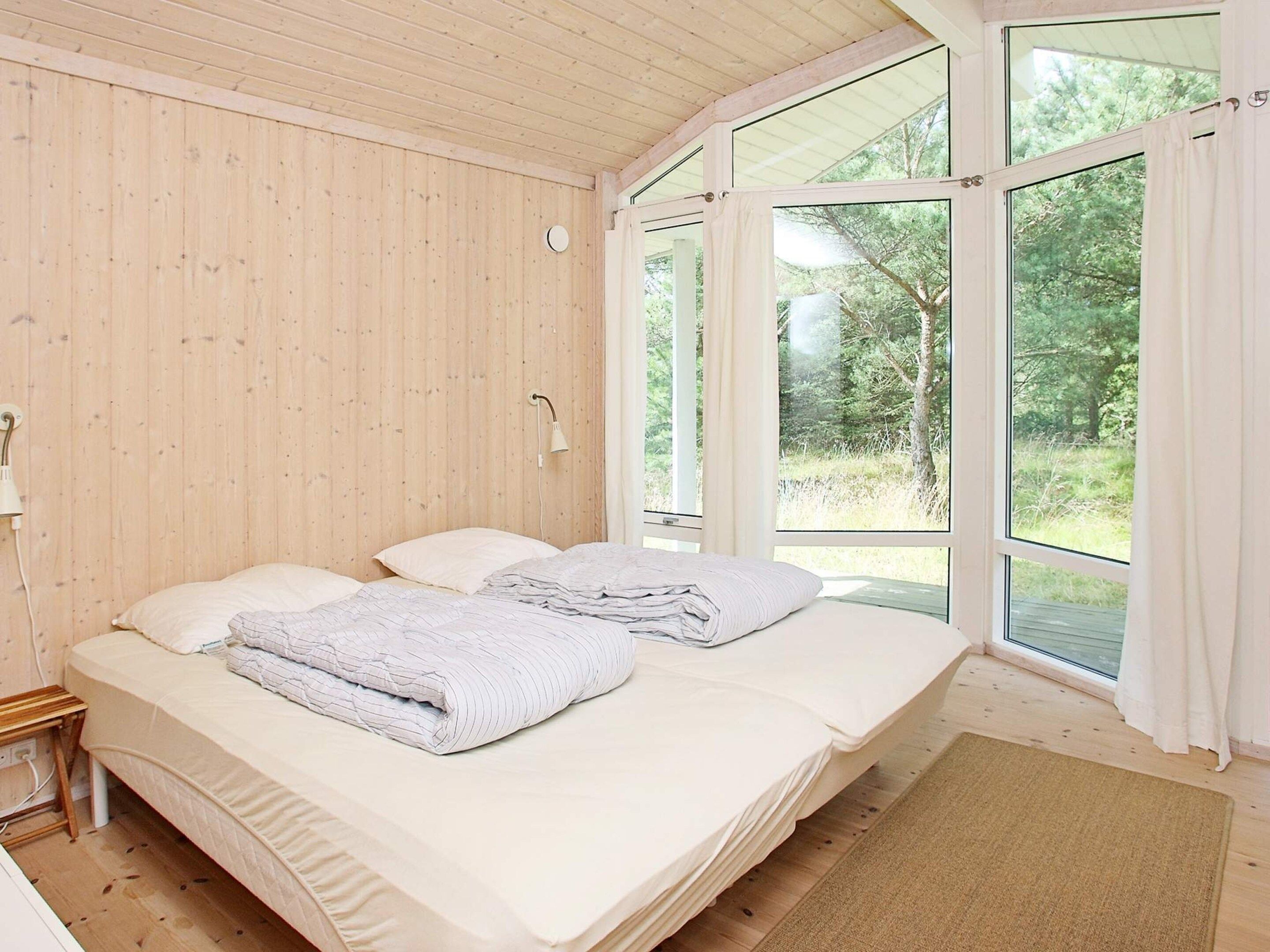 Un dormitorio con techo de madera, una cama con ropa de cama blanca, una mesita de noche y un ventanal con cortinas.
