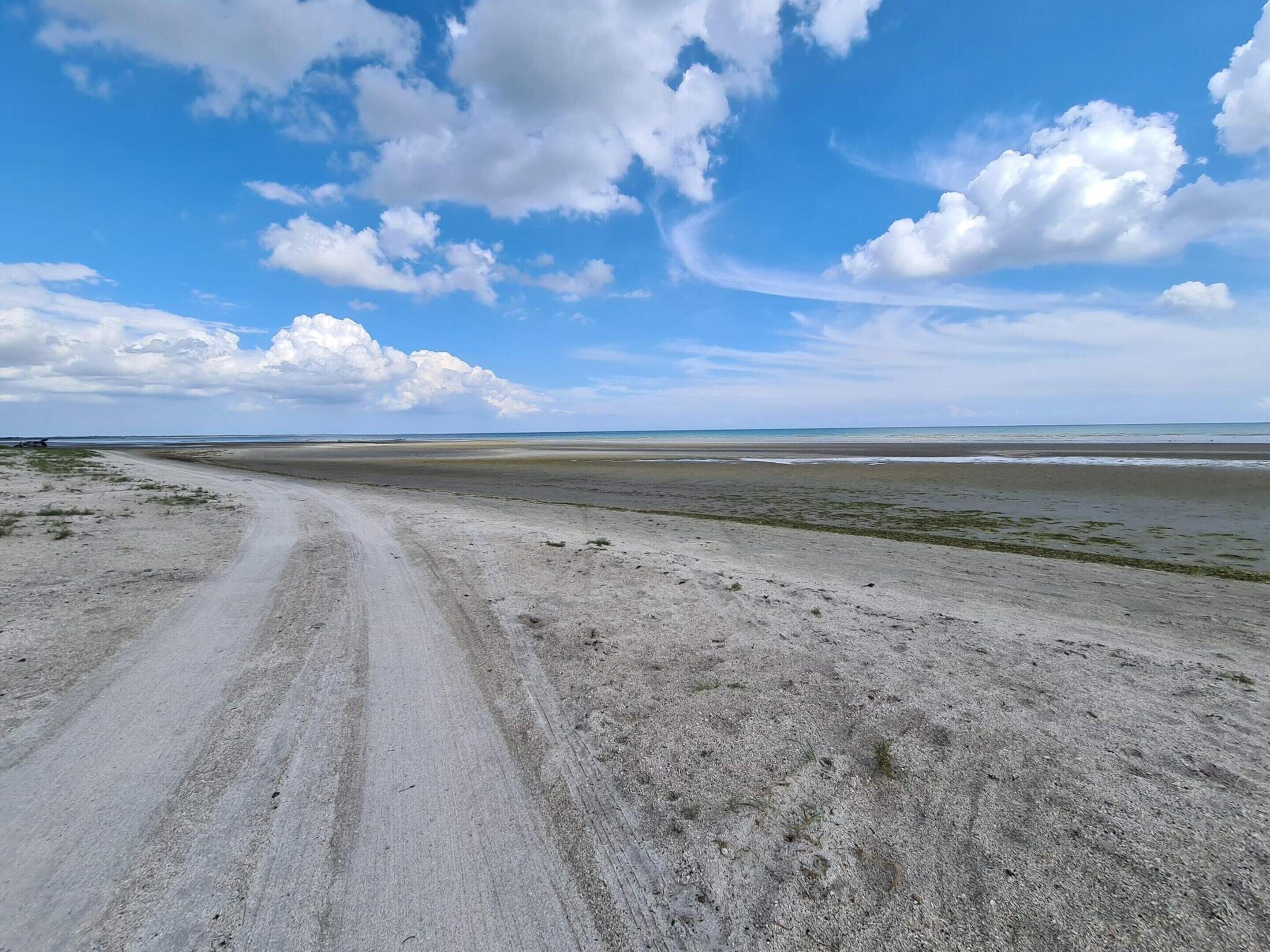 A wide, open landscape with a dirt road leading towards a distant shoreline.