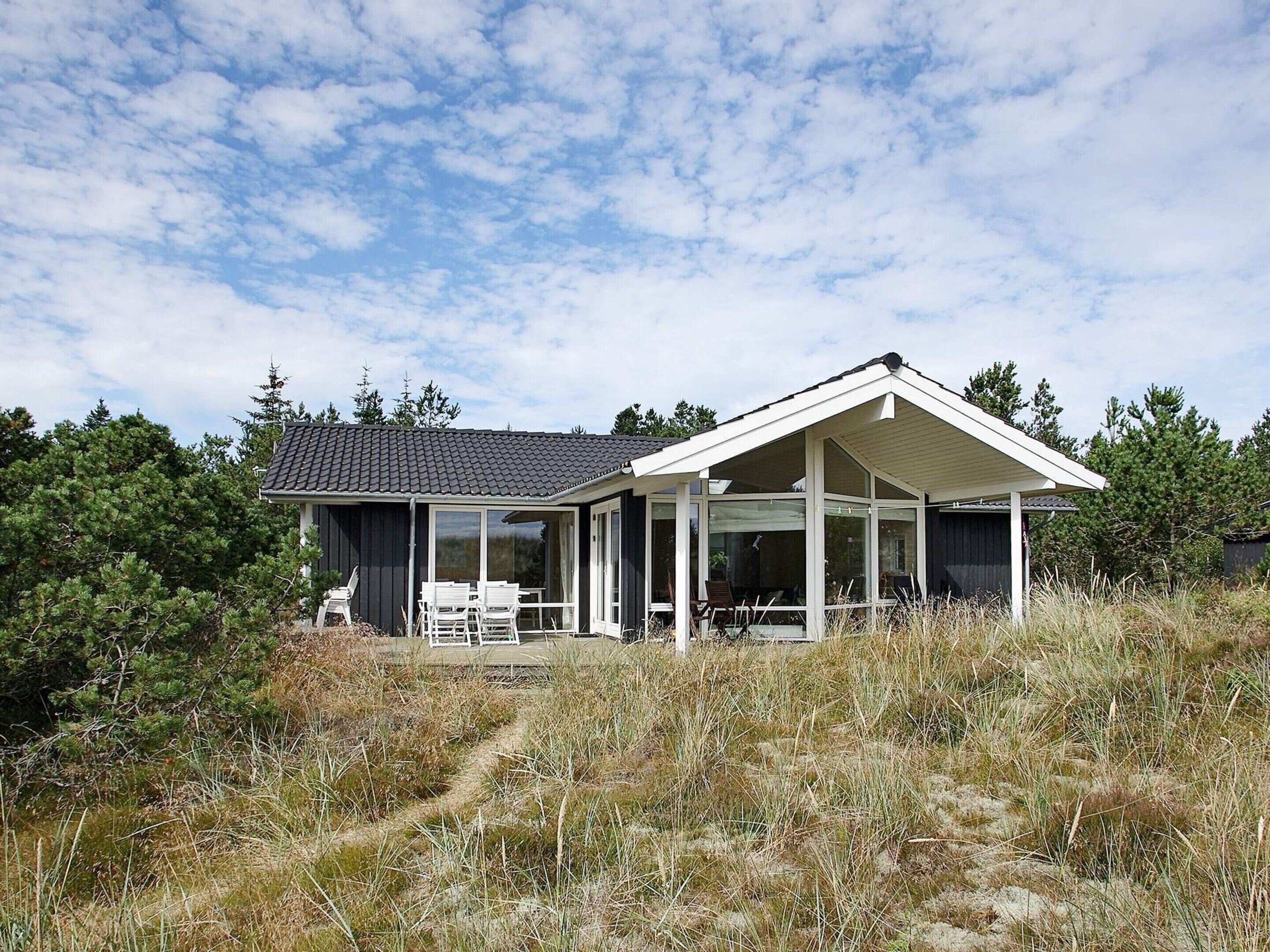 A modern house with a covered patio, surrounded by natural vegetation.