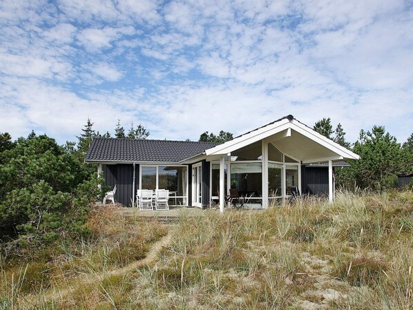 A modern house with a covered patio, surrounded by natural vegetation.