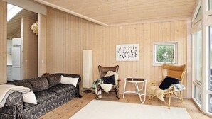 A cozy room with a wooden ceiling, a patterned sofa, two wicker chairs, a small white table, and a large window. - 4 Star Holiday Home in Jerup (Jerup)
