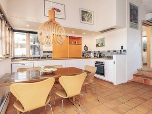 A modern kitchen with a central island, white cabinetry, and a dining area with a wooden table and chairs.