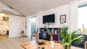Olohuoneessa on puinen ruokapöytä, seinälle asennettu televisio ja ikkuna, jossa on verhot.
