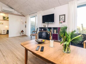 Een woonkamer met een houten eettafel, een aan de muur bevestigde televisie en een raam met gordijnen.