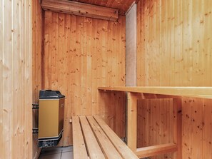 A wooden cabin interior with a bench, a small table, and a heater.
