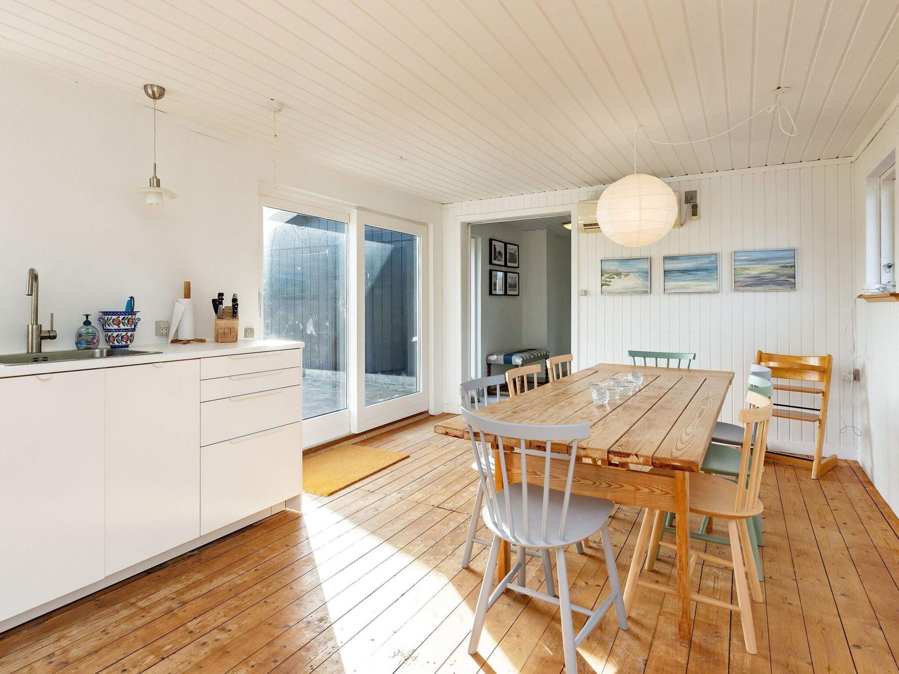 Et rummeligt køkken med et stort træbord og stole, en hvid bordplade og en skydedør til en balkon.