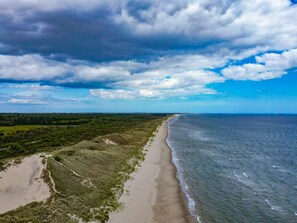 Un paysage côtier avec une plage de sable, des dunes herbeuses et une vue sur l’océan sous un ciel partiellement nuageux.