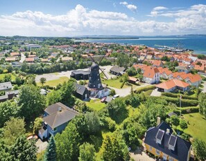 A coastal village with traditional windmills, houses with red roofs, and a large body of water in the background.