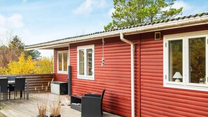 A red wooden house with a deck, outdoor seating, and a window with a lamp. - 4 Person Holiday Home in Ebeltoft-by Traum (Ebeltoft)