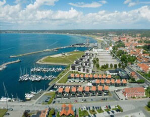 An aerial view of a coastal town with a marina, modern buildings, and a red-roofed structure.