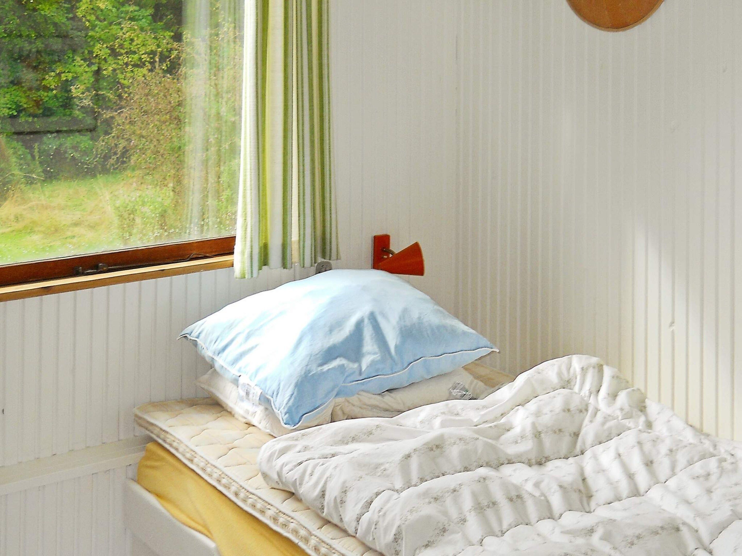A bedroom with a bed, a window with curtains, and a wall-mounted lamp.