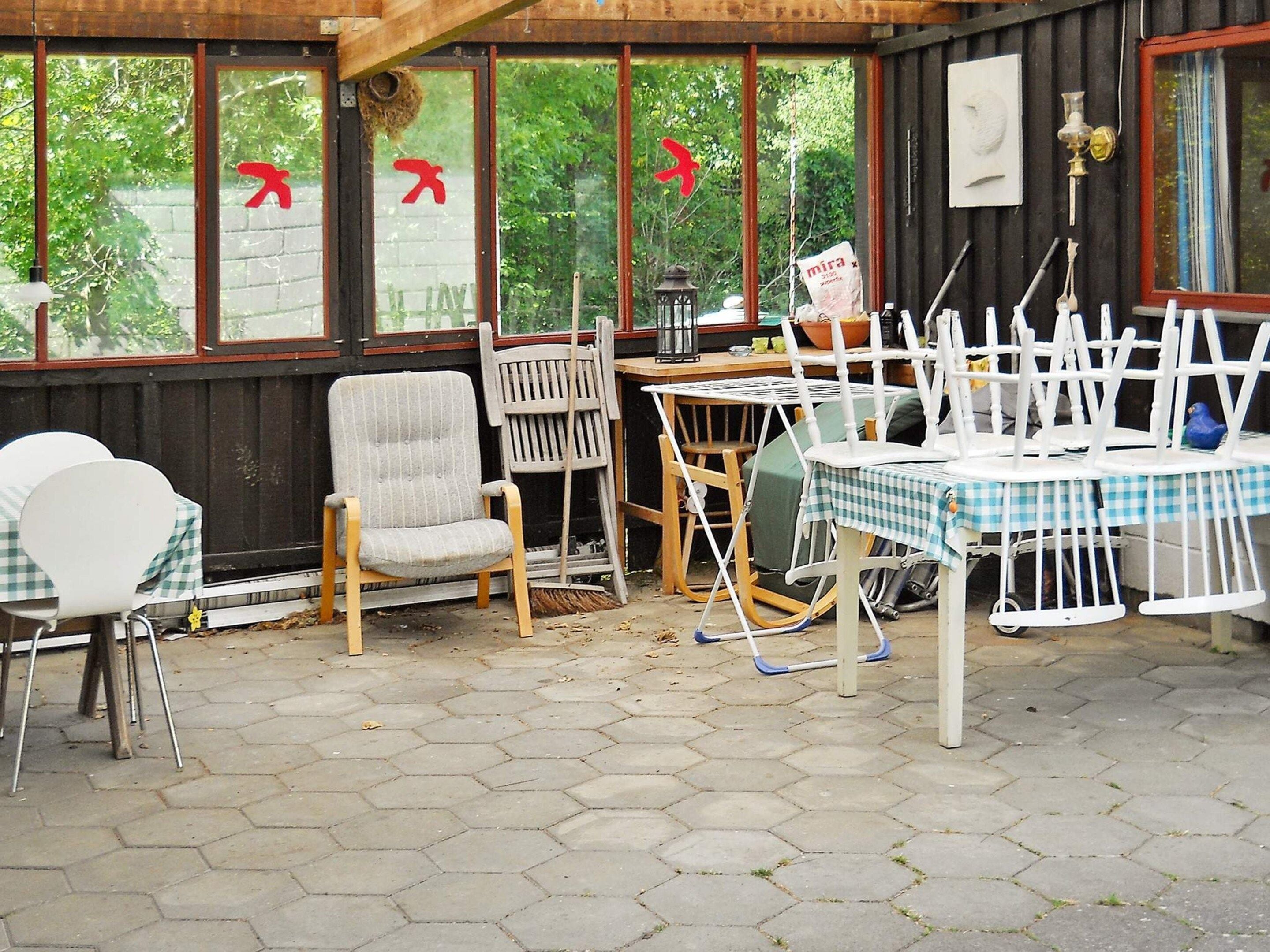 A covered outdoor seating area with hexagonal tiles, wooden chairs, and a table with a checkered tablecloth.