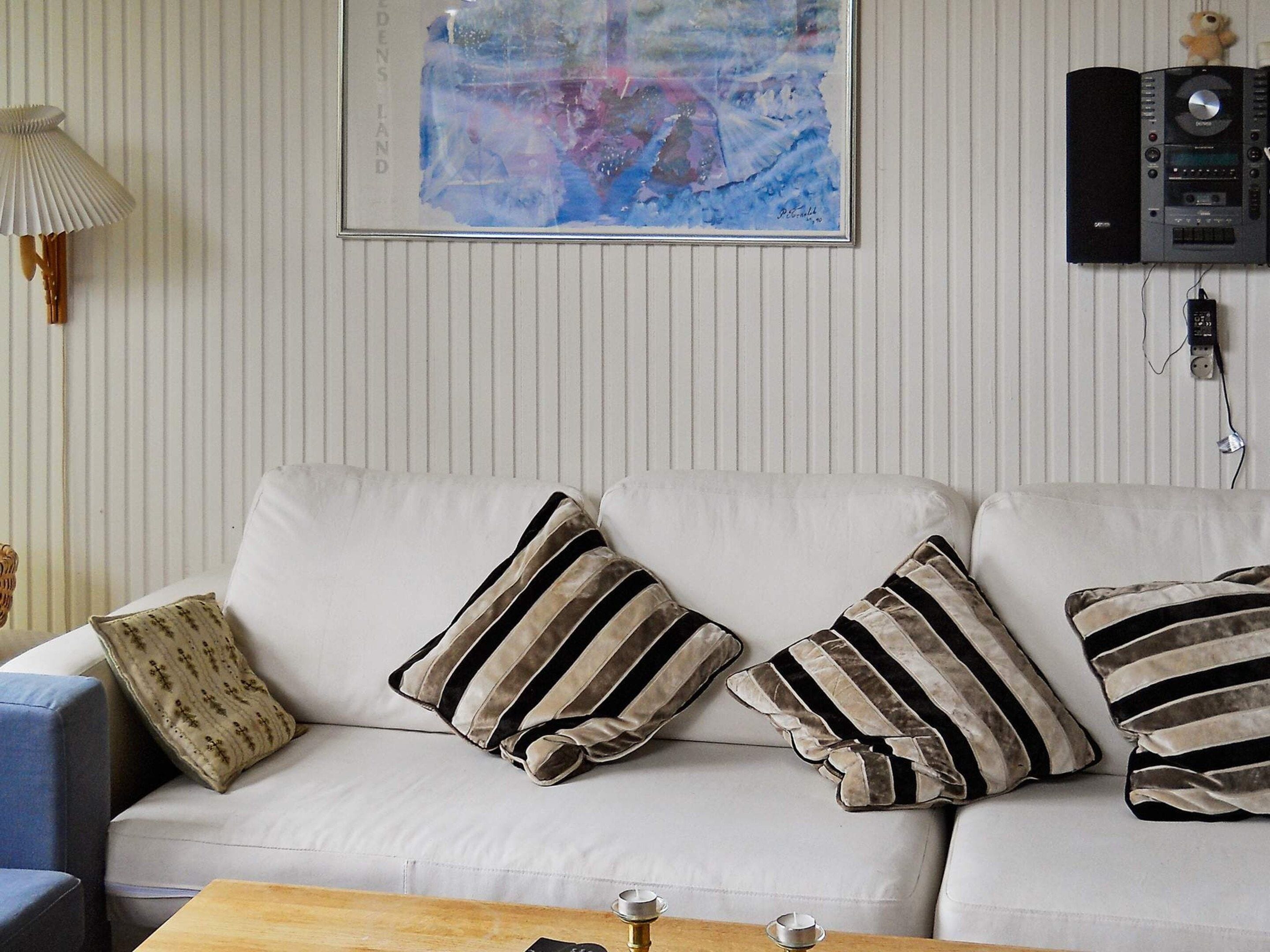 A living room with a sofa, striped pillows, a lamp, a painting, and a stereo system.