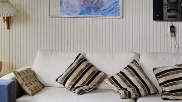A living room with a sofa, striped pillows, a lamp, a painting, and a stereo system.