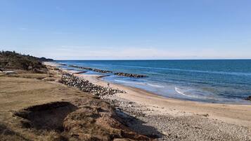 A coastal landscape with a pebbly beach, a rocky breakwater, and a clear sky.