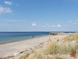 A beach with pebbles, grass, and a rocky outcrop.
