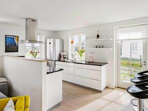 A modern kitchen with white cabinets, stainless steel appliances, and a dining area with a yellow chair and a black bar stool.