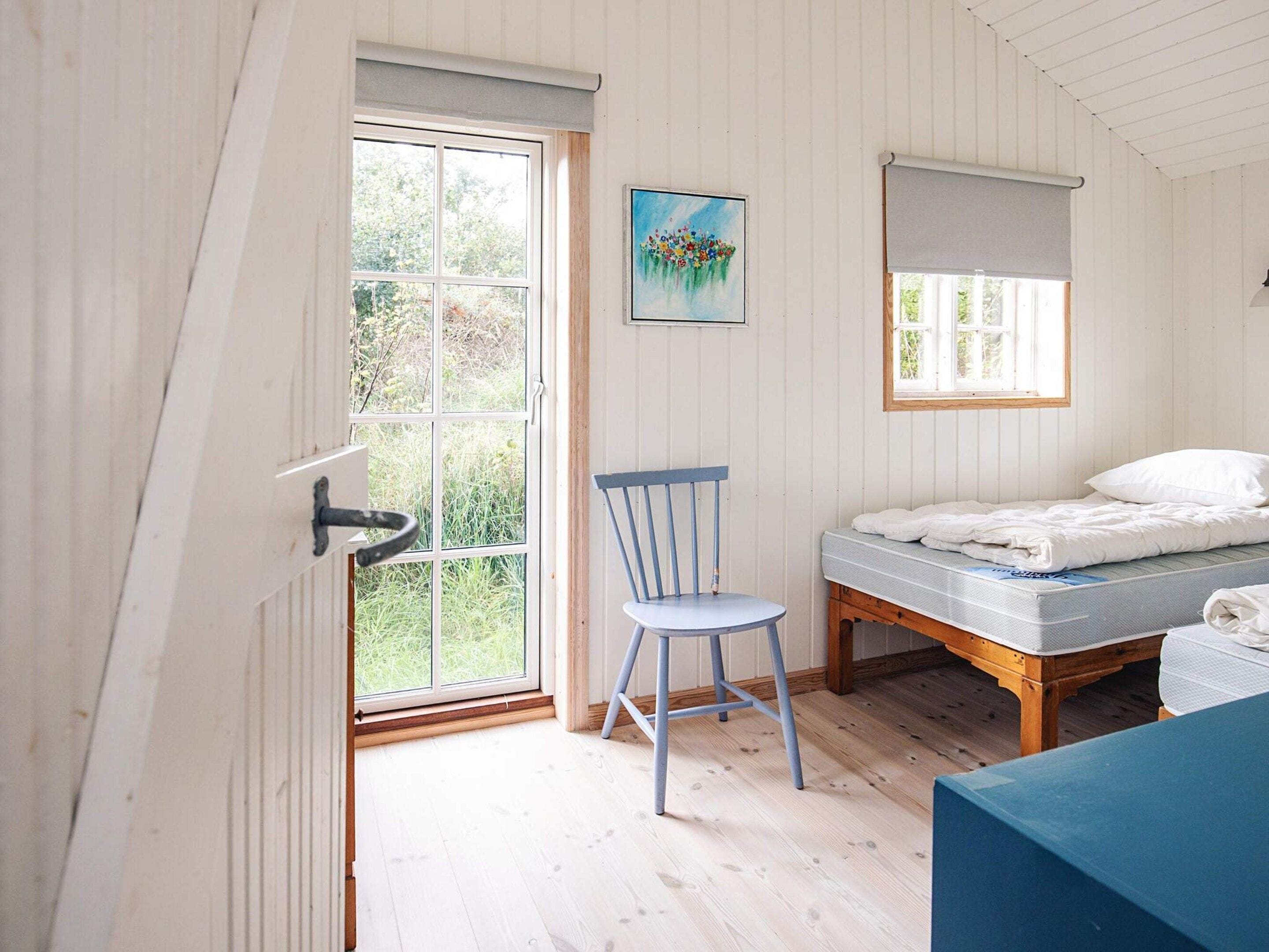 Una habitación con una cama, una silla, un ventanal y un cuadro en la pared.
