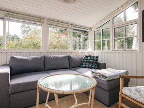A room with a grey sectional sofa, a round glass-top table, and a wicker chair.