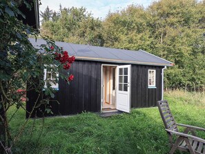 A small wooden cabin with a door open, surrounded by grass and trees. - Serene Holiday Home in Bindslev near Beach (Bindslev)