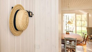 En halmhat hænger på en hvid væg i et rum med trægulv og et bord med stole.