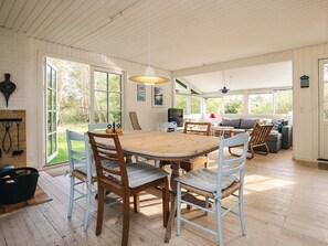 A spacious room with a wooden dining table, chairs, a sofa, and a television.