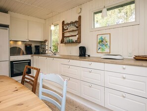 A kitchen with white cabinetry, a wooden countertop, a stove, and a dining table with chairs. - Serene Holiday Home in Bindslev near Beach (Bindslev)